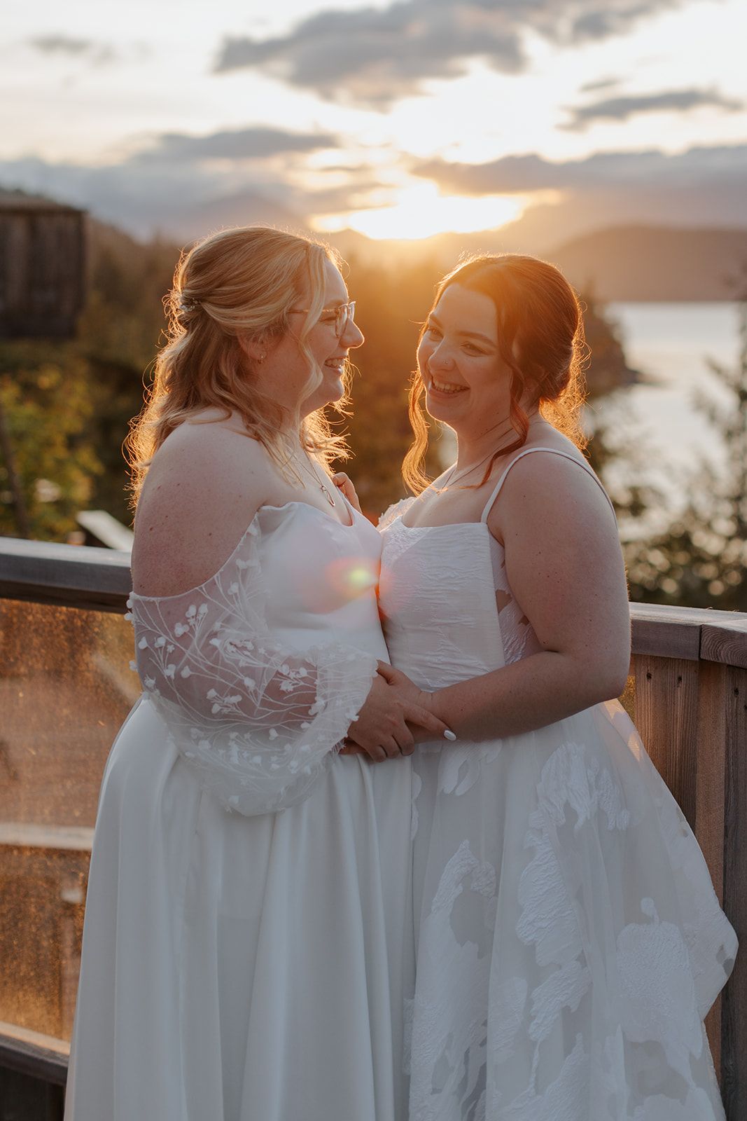 Three people in white dresses share an intimate moment at sunset on a mountain deck.