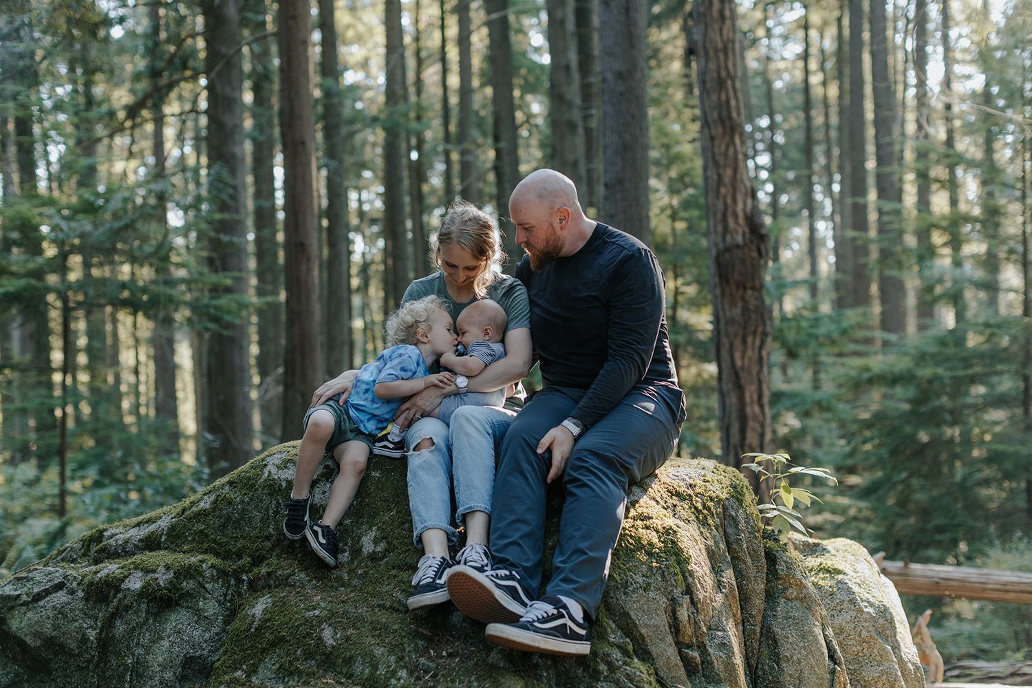 Family sitting together on rocky outcrop in serene forest setting.