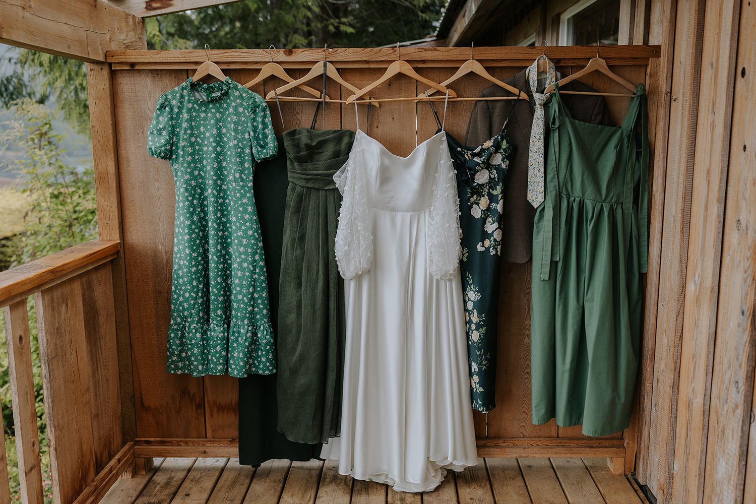 Collection of green and white dresses hanging on wooden hangers in rustic setting.