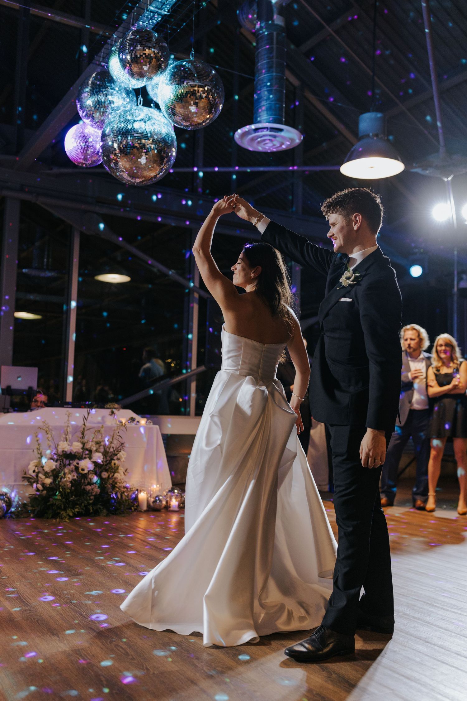Couples dancing beneath sparkling disco balls at an elegant wedding reception on a polished wooden dance floor.