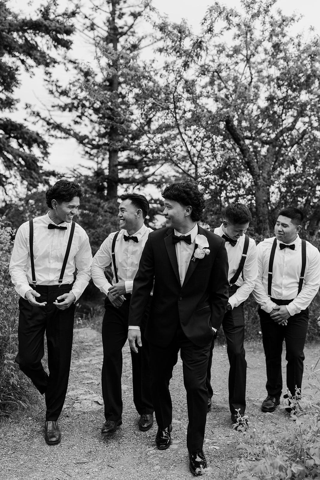 Groomsmen in formal attire and suspenders walking together in a casual outdoor setting.