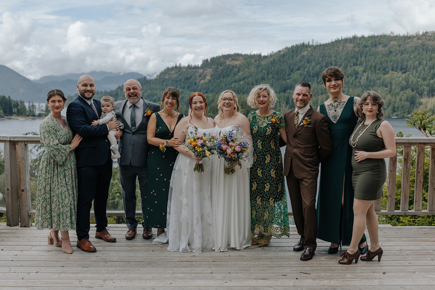 Wedding party poses together on scenic outdoor deck overlooking mountain lake landscape.
