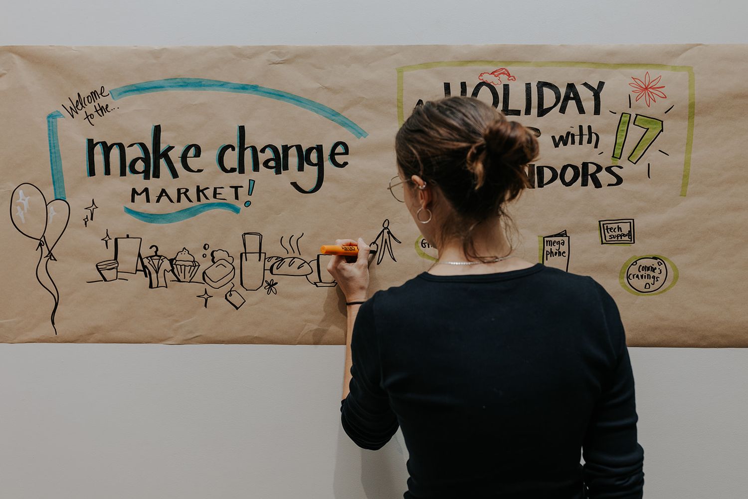 Handwritten signs and decorative text displayed on a beige wall at a holiday market.