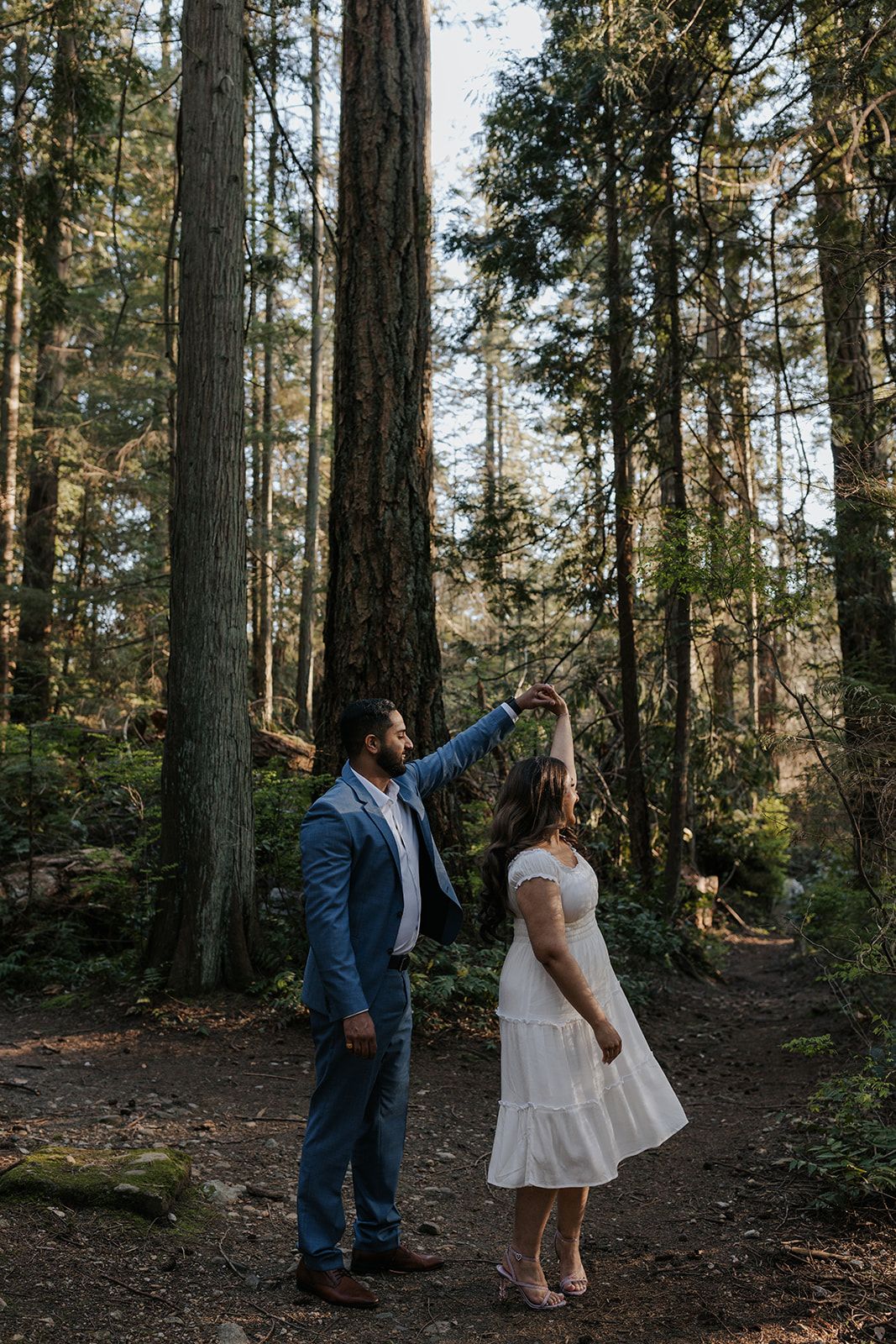Couple enjoying a playful moment among tall trees in a forest.