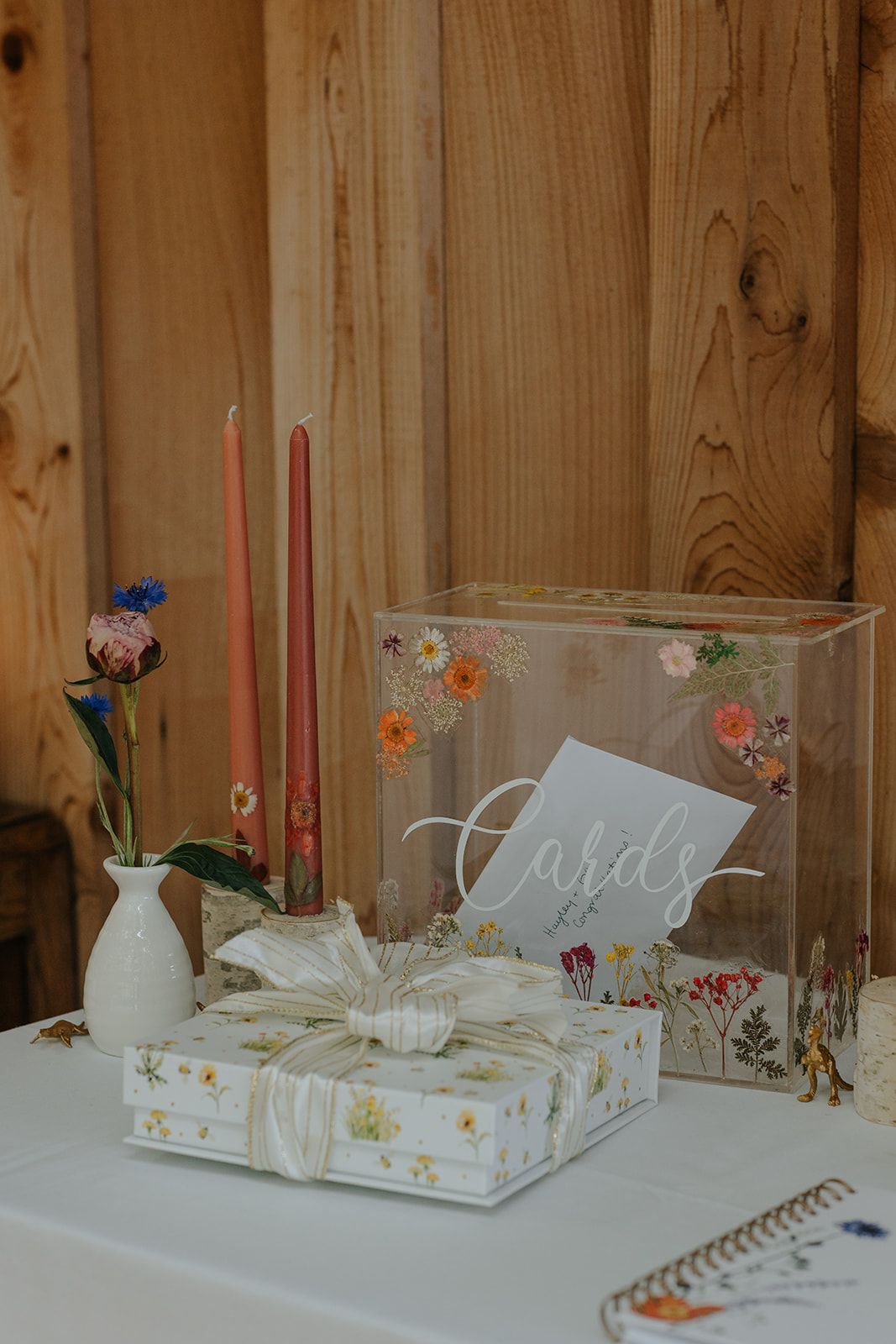 Wedding gift display with decorated glass box, candles and floral wrapping paper on white surface.