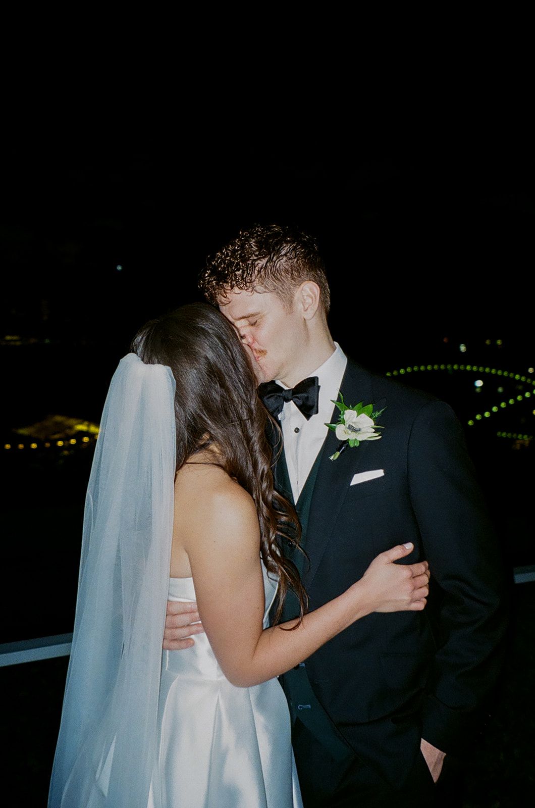 Romantic nighttime wedding portrait with city lights in background.