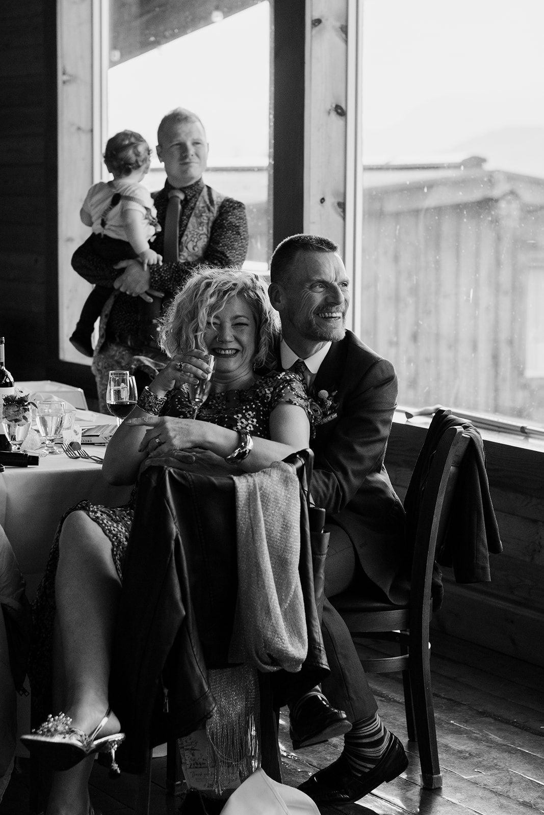 Candid moments captured in black and white of guests enjoying themselves by large windows.