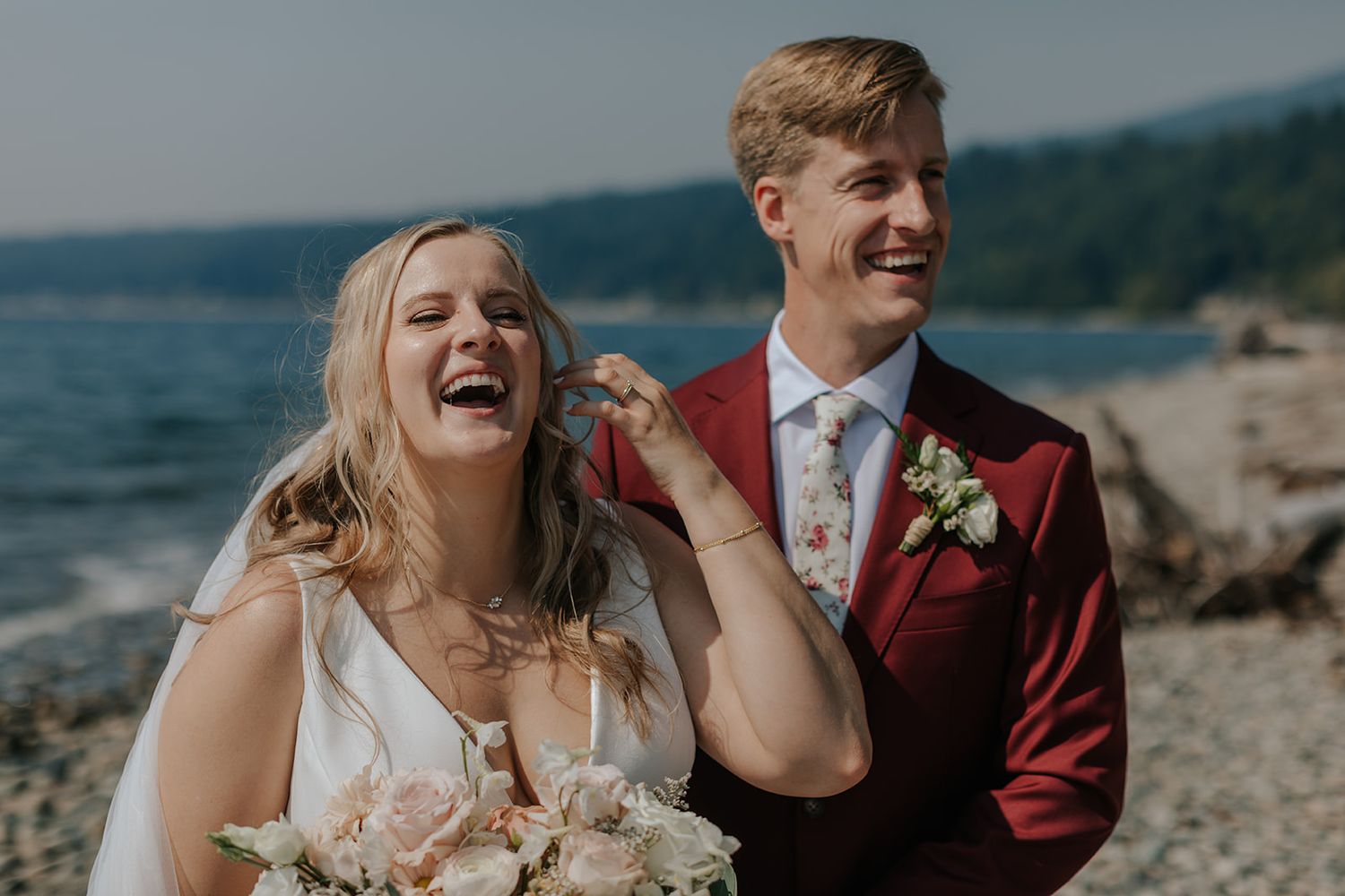 Candid wedding photos of a couple laughing together on a beach with water in the background.