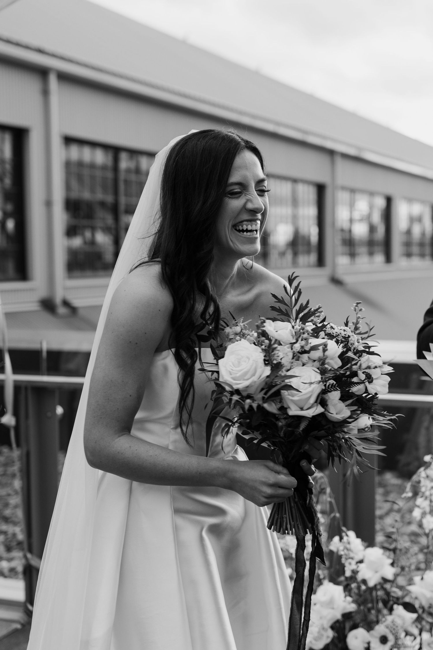 Candid moment of bride laughing while holding white and green floral bouquet.