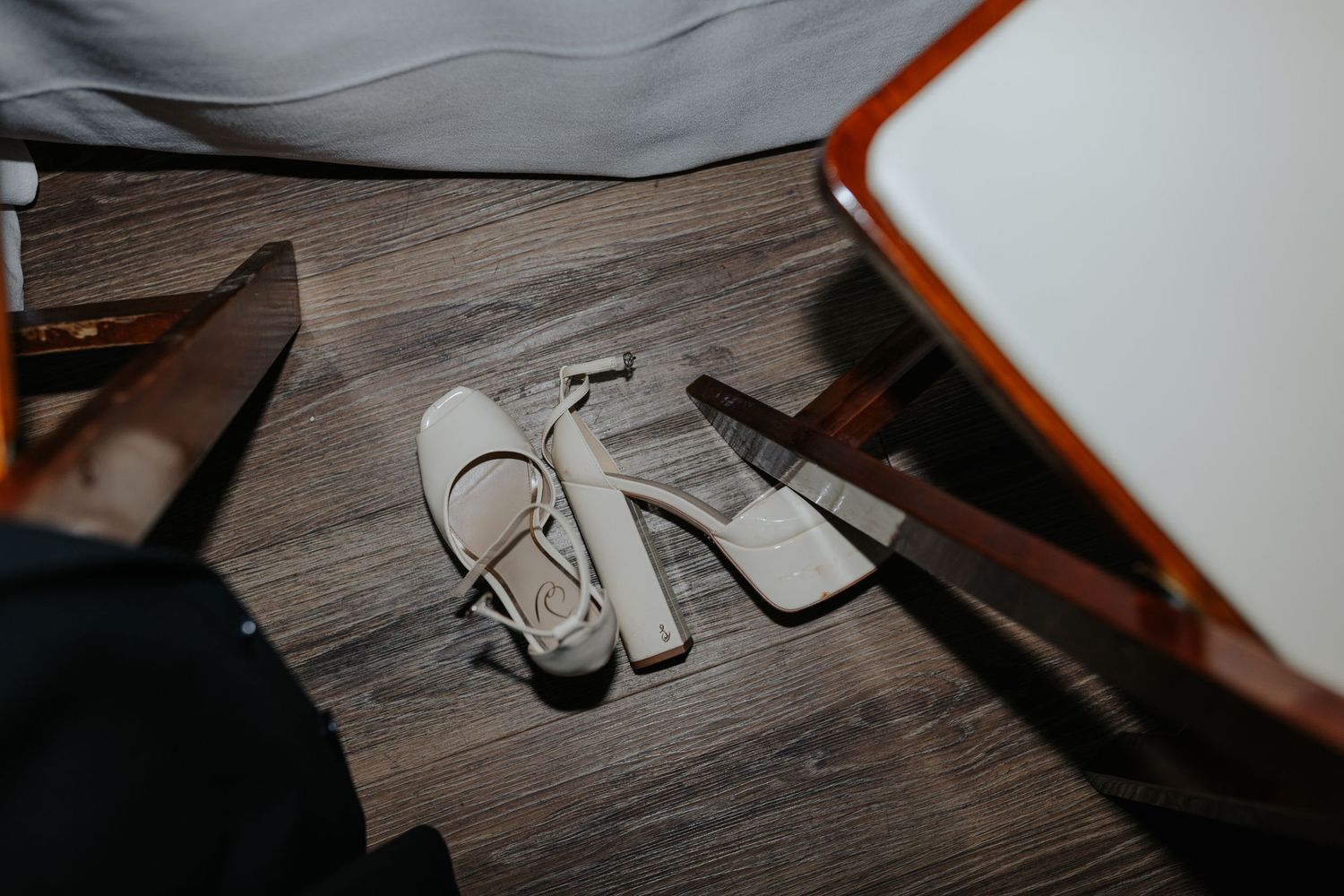 White shoes rest on a dark wooden floor surface in low lighting conditions.