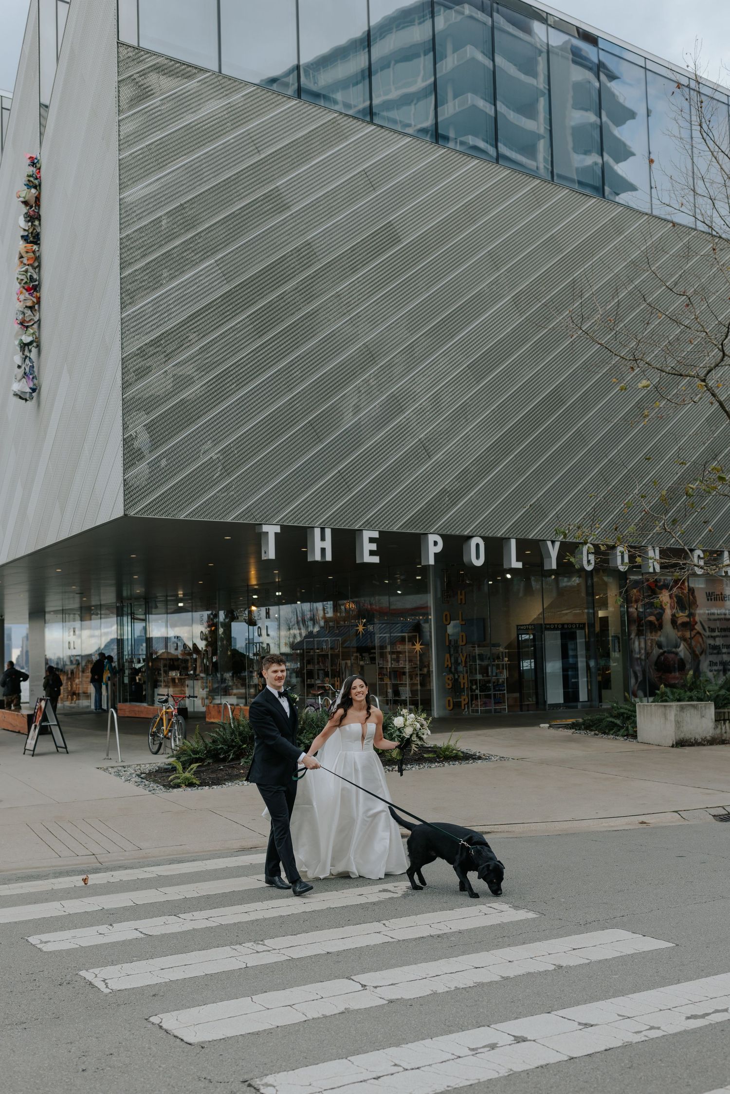 A couple poses for wedding photos in front of a modern building with glass windows and white columns.