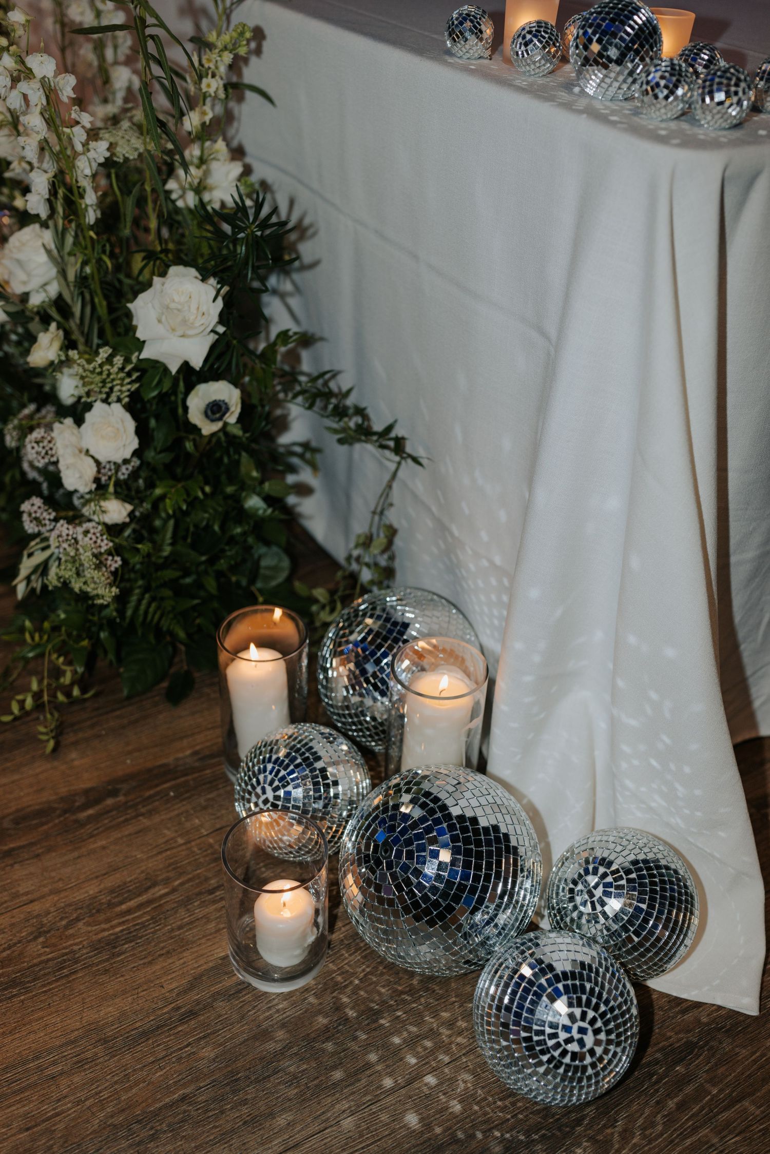 Disco balls and white candles create a glamorous floor decoration against wooden flooring.