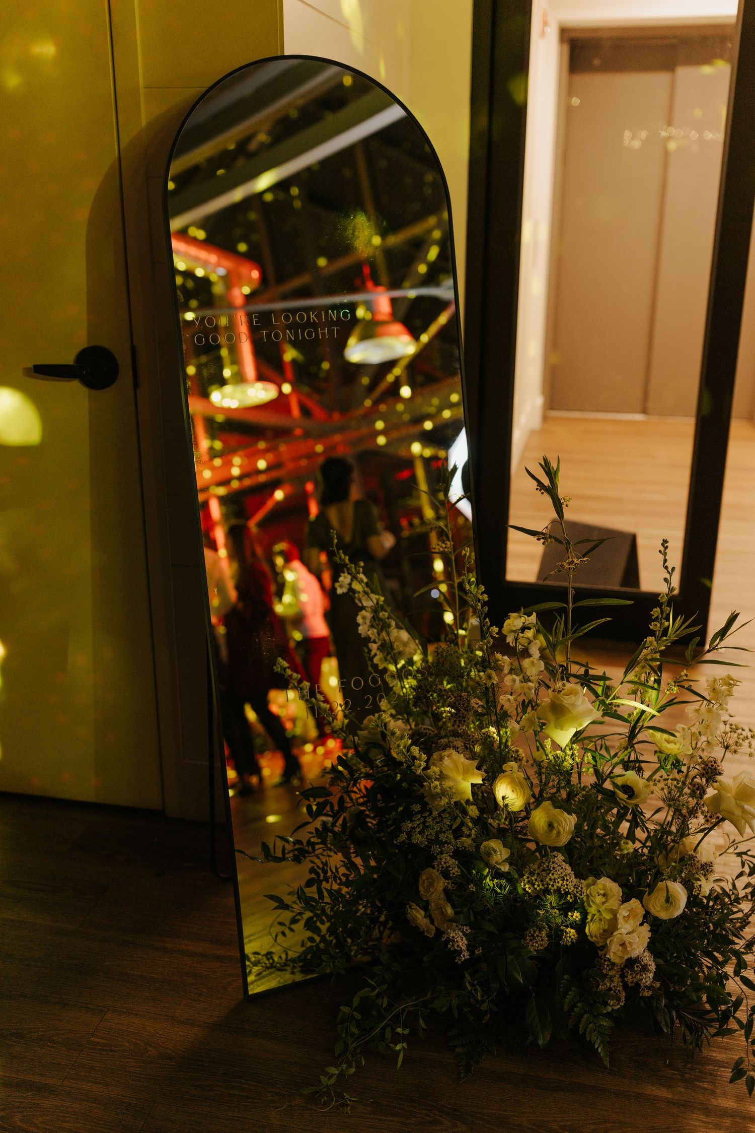 Elegant floral arrangements with white flowers and greenery decorate a dimly lit indoor venue space.