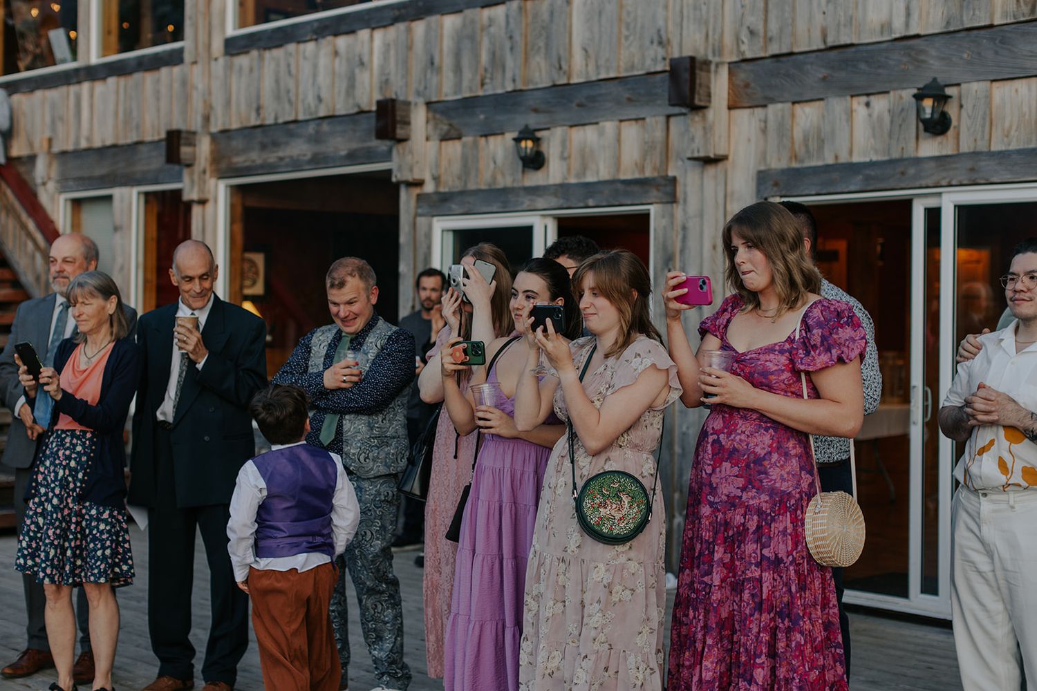 Wedding guests mingle on a rustic deck during an outdoor reception.