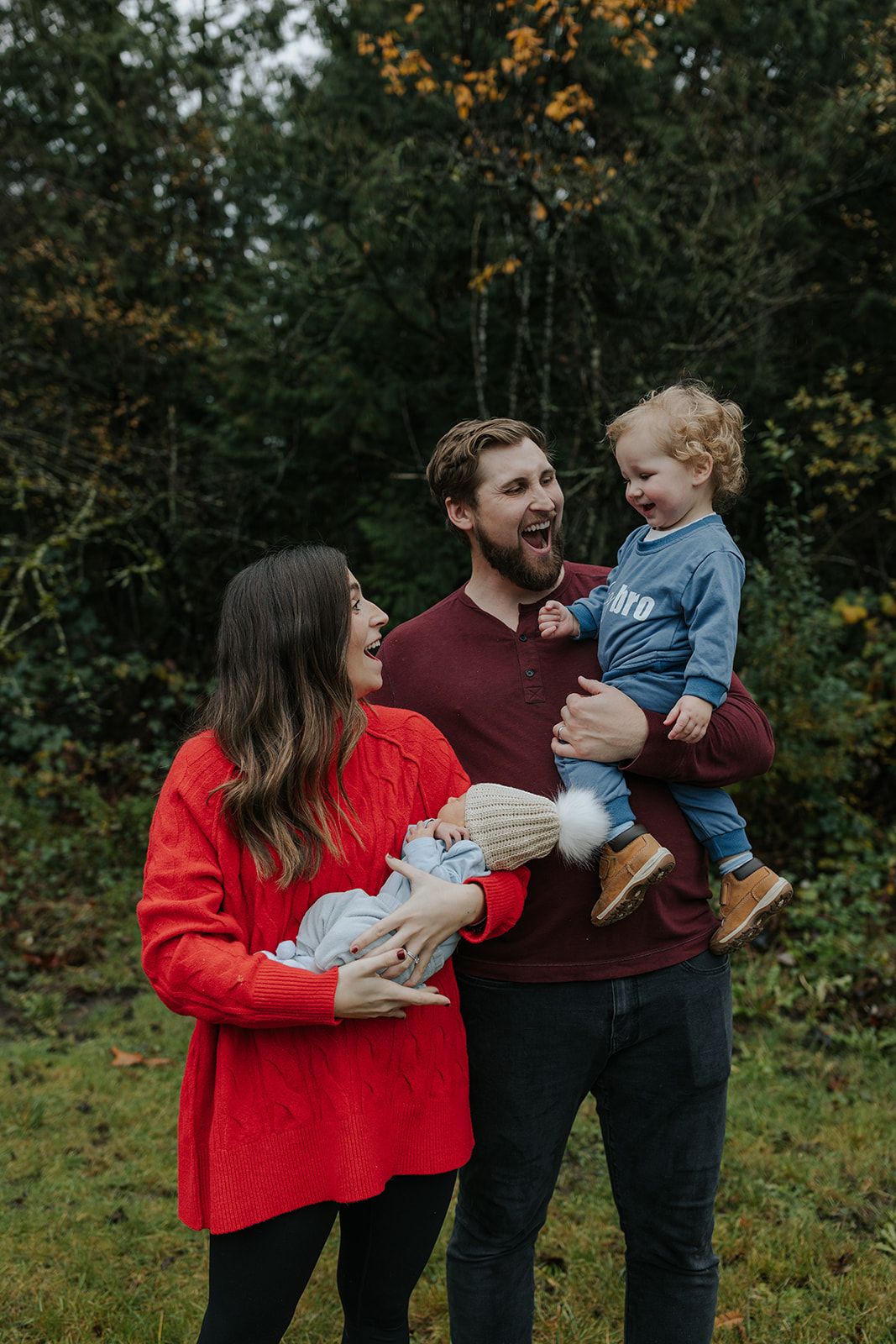 A family of four poses together outdoors during autumn with fall foliage in the background.