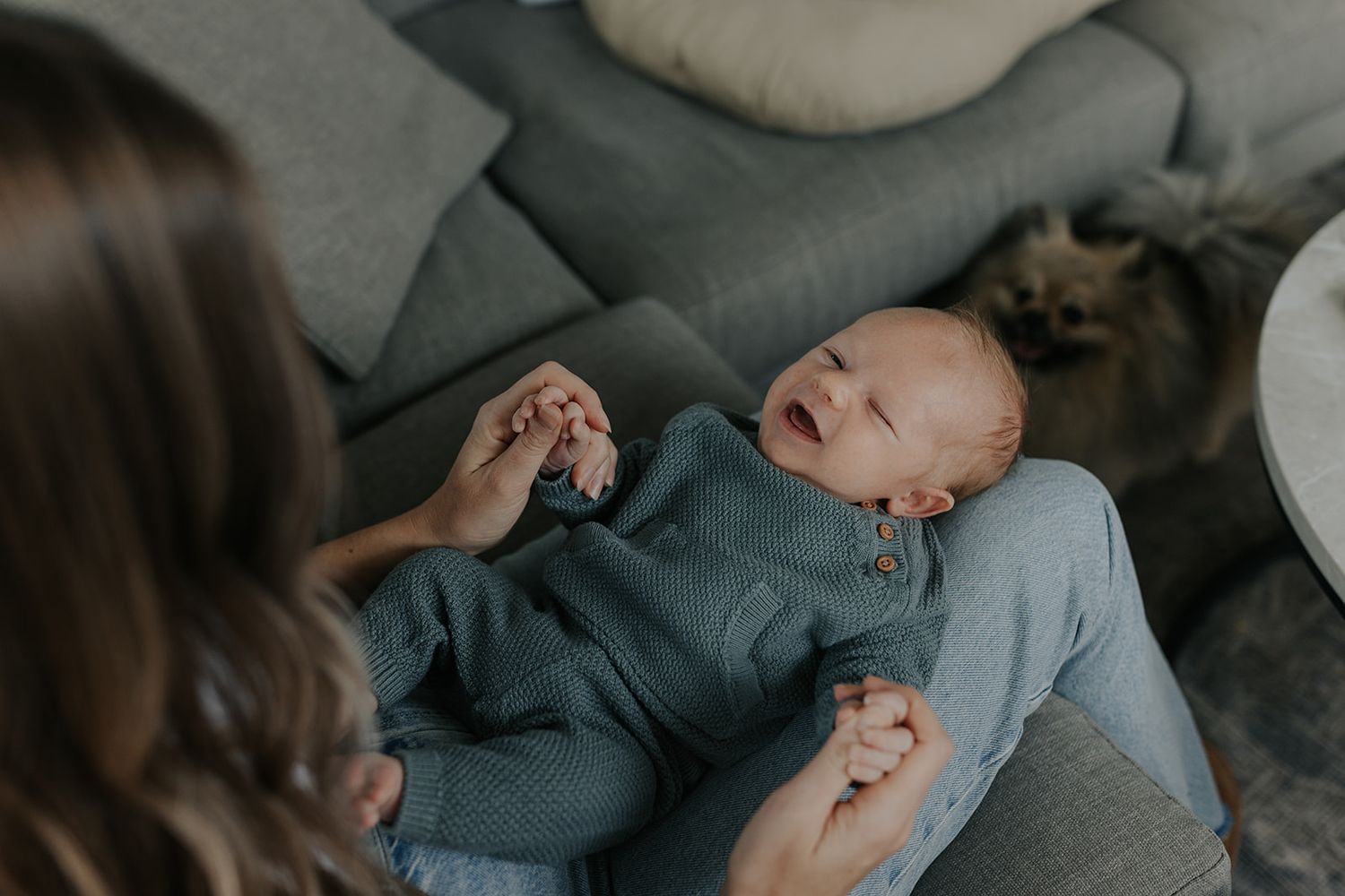 Candid family moments captured on grey couch in moody lighting.