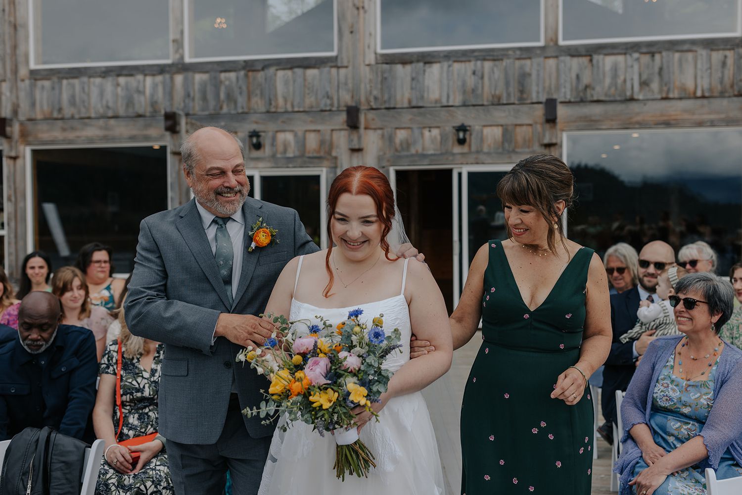 Wedding celebration with guests on wooden deck under cloudy mountain skies.