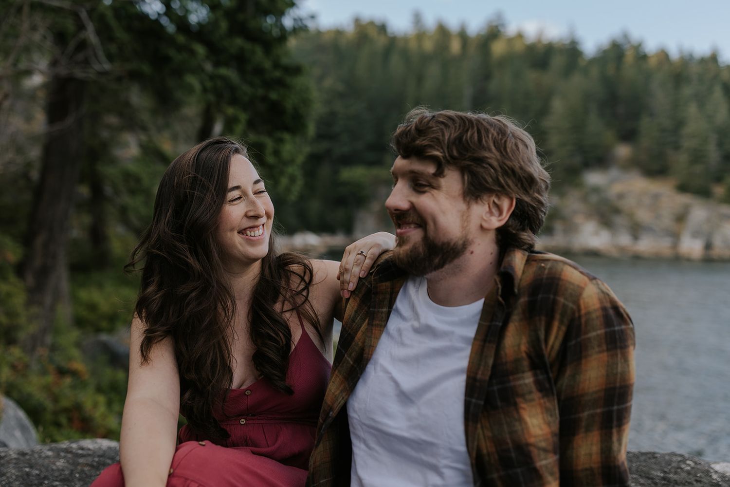 Couple shares romantic moments by a scenic lakeside surrounded by evergreen trees.