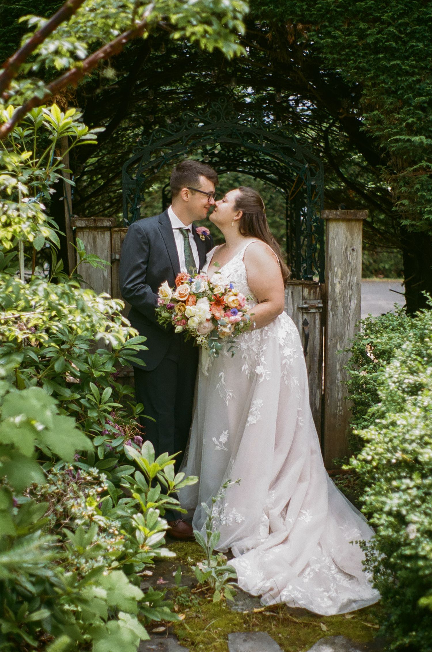 A romantic wedding couple shares a tender moment in a lush garden setting with a beautiful floral bouquet.