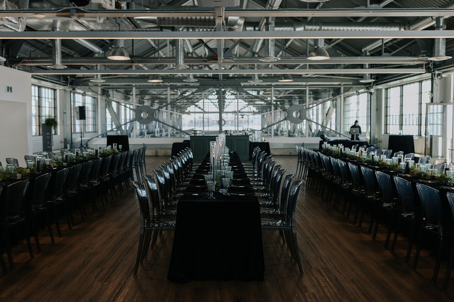 Empty reception hall with rows of black chairs and tables set for an elegant event.