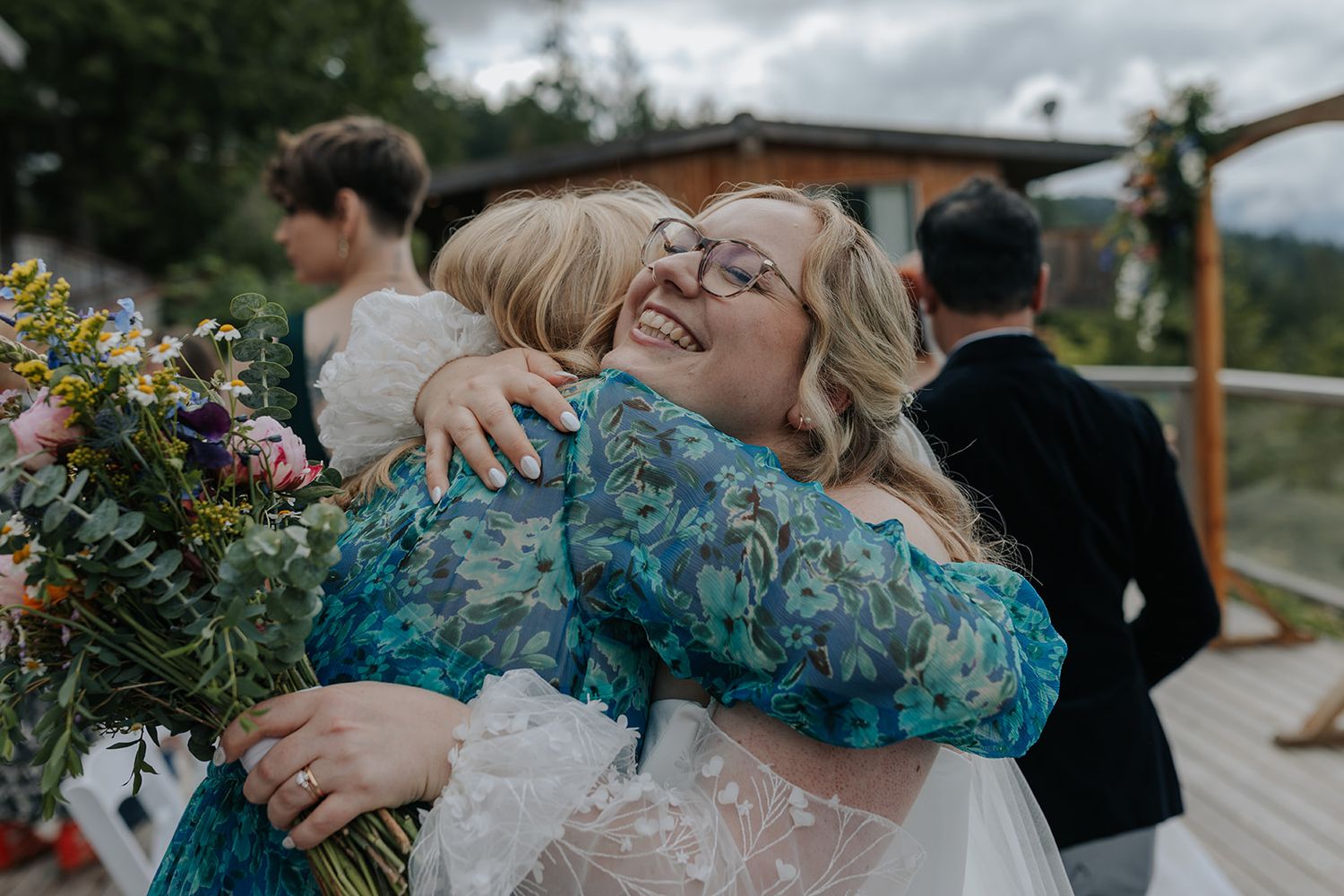 Wedding guests embrace during outdoor celebration with mountain scenery.