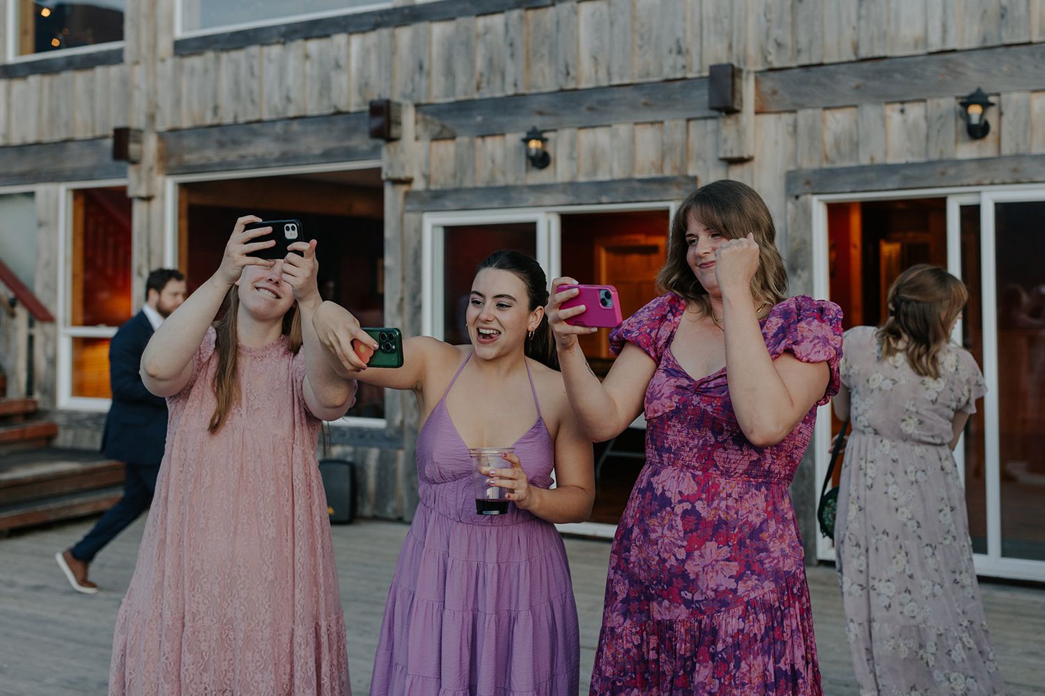 Wedding guests in pink and purple dresses share laughs during outdoor reception.