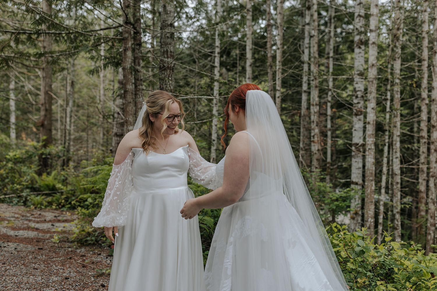 Two brides share an intimate moment surrounded by tall evergreen trees.