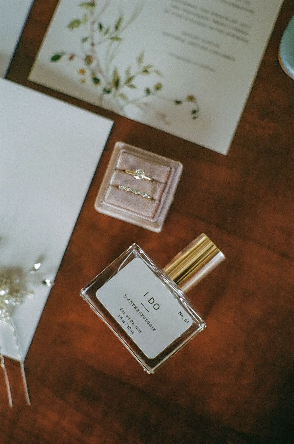 Perfume bottles and wedding stationery with floral designs on wooden surface.