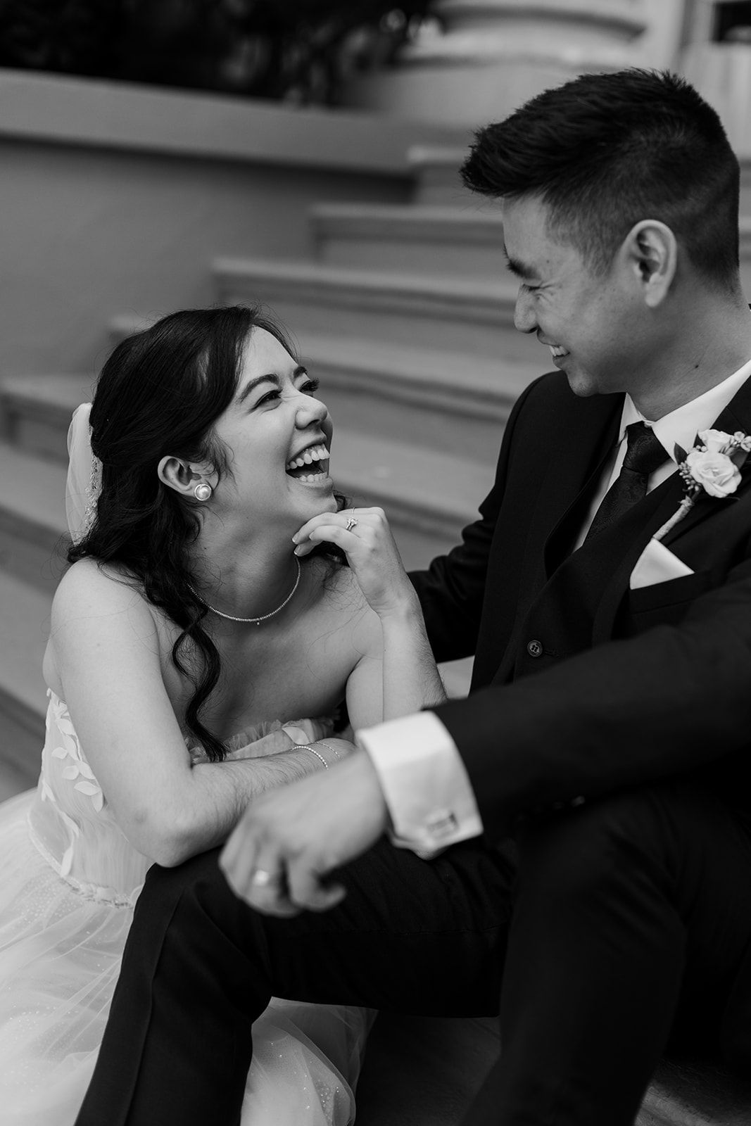 Black and white photo of a couple sharing a joyful moment in formal attire.