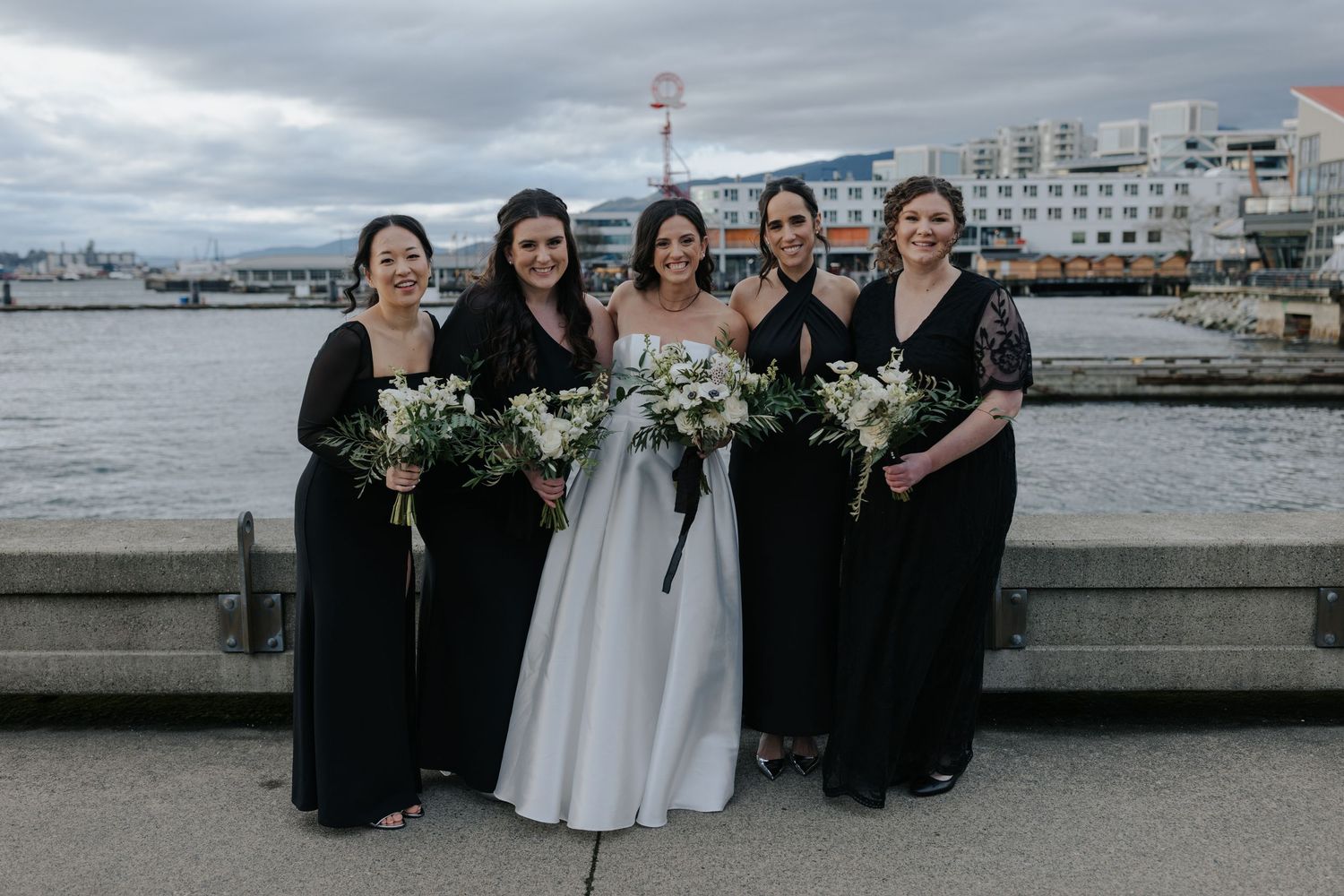 Wedding party in formal black and white attire poses together on a waterfront pier.