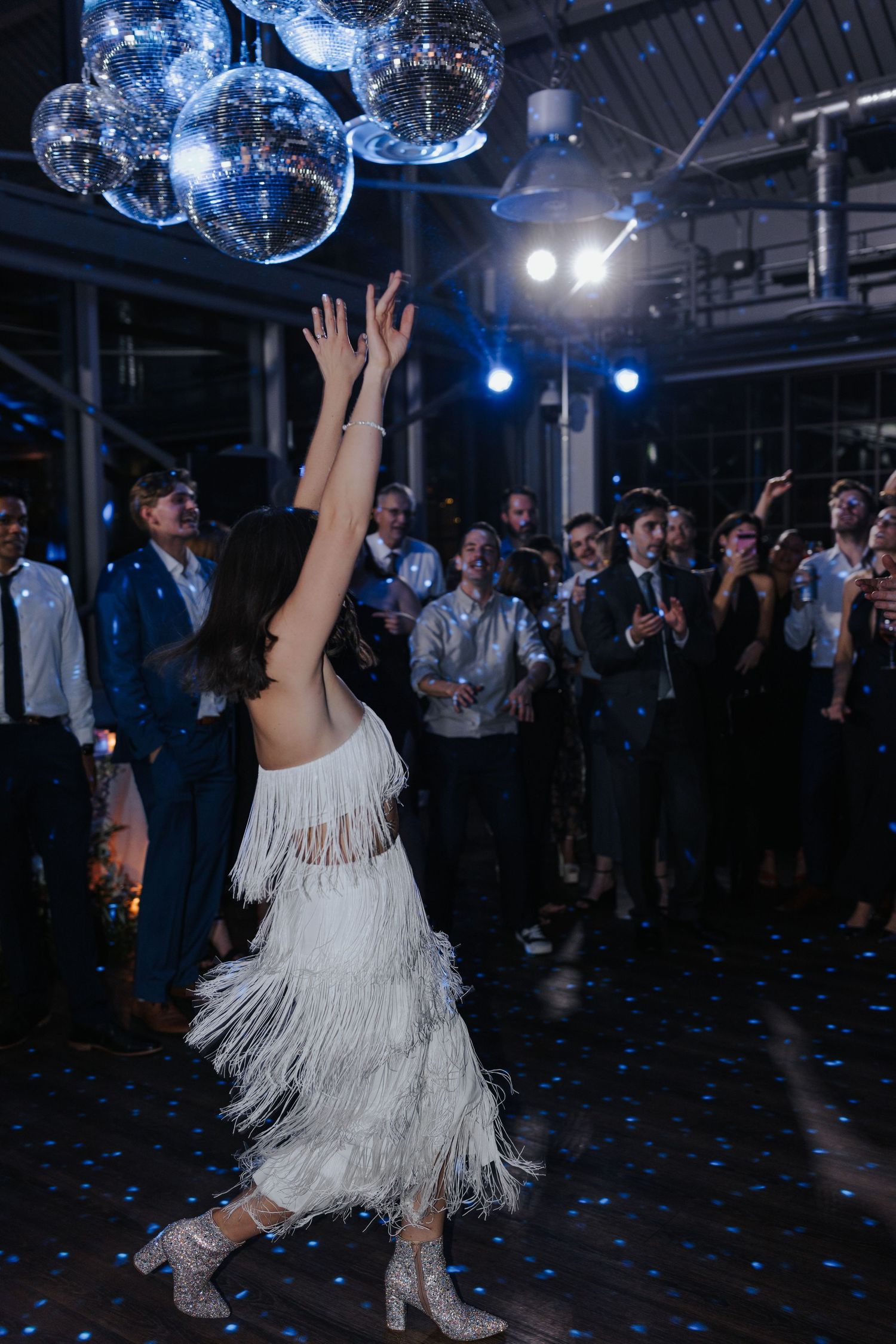 Dance floor scene with disco balls casting blue light and confetti scattered across the floor during a celebration.