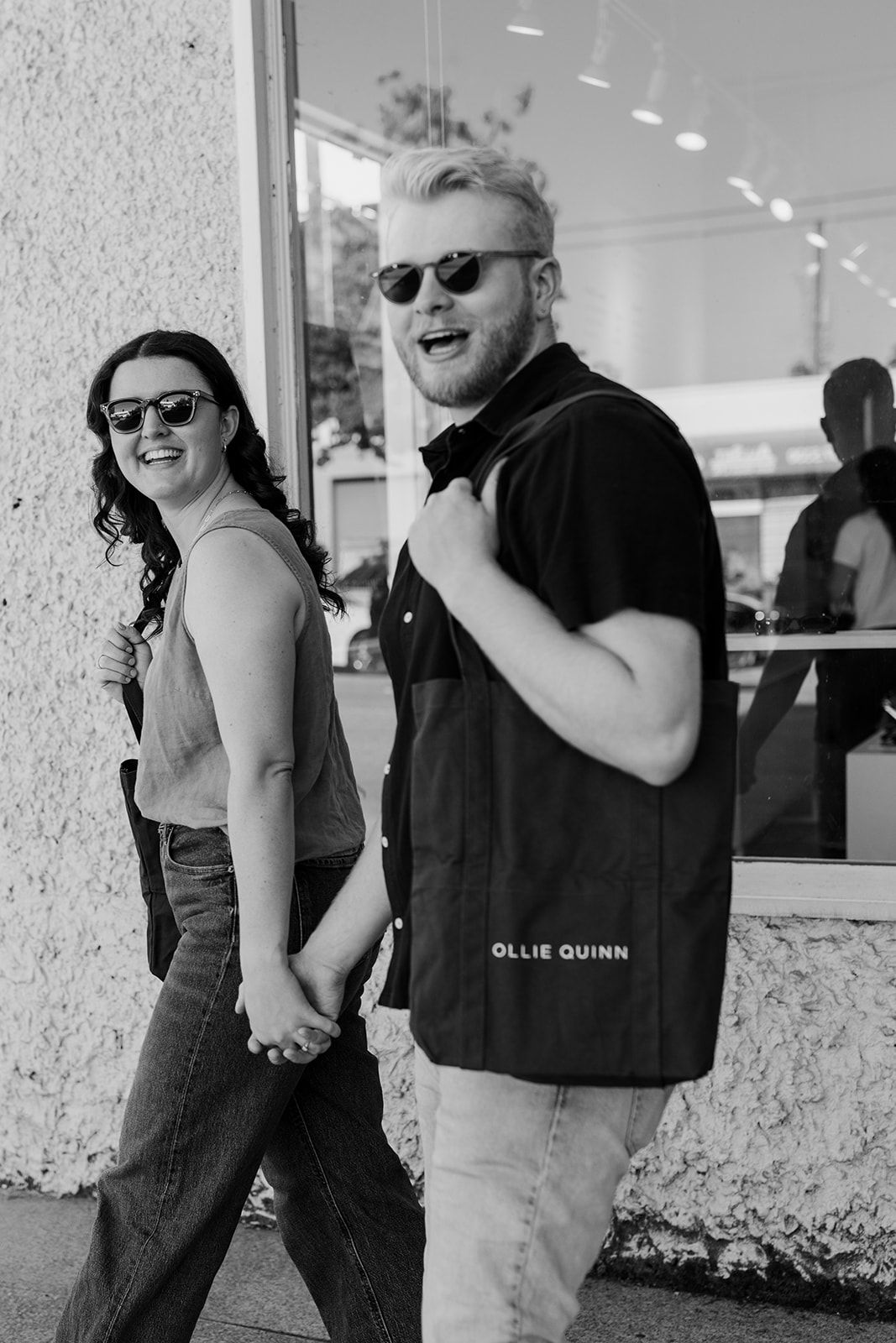A couple shares playful moments together outside a modern building in black and white photography.
