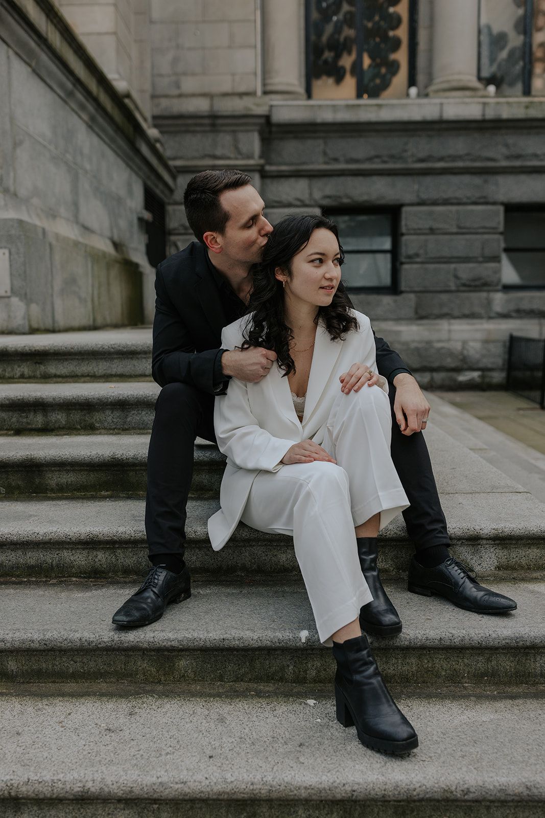 A couple sits intimately on stone steps of a historic building with architectural details.