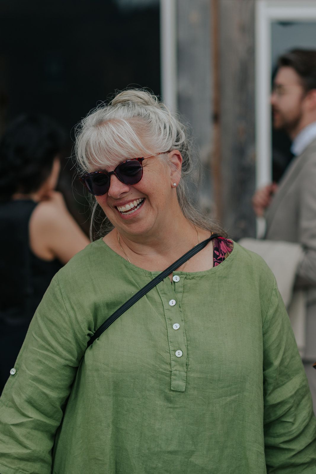 Guest in green linen shirt smiling during outdoor wedding celebration.