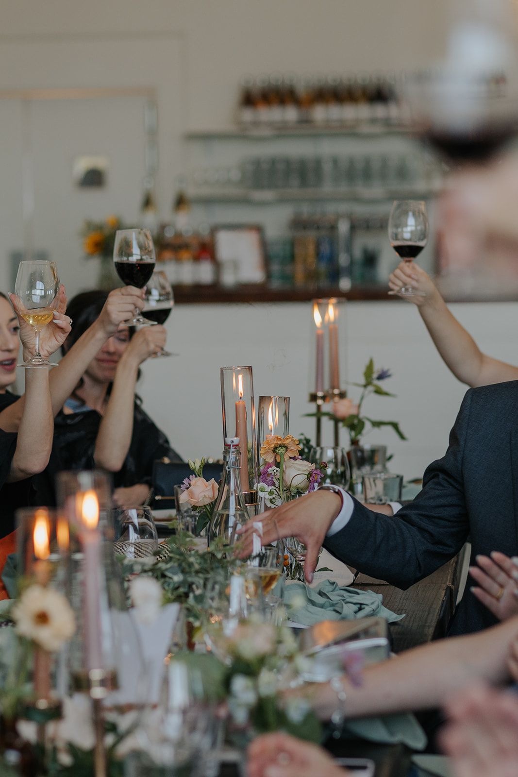 People raising wine glasses in a toast at an elegant dinner party with candlelight and floral table decorations.