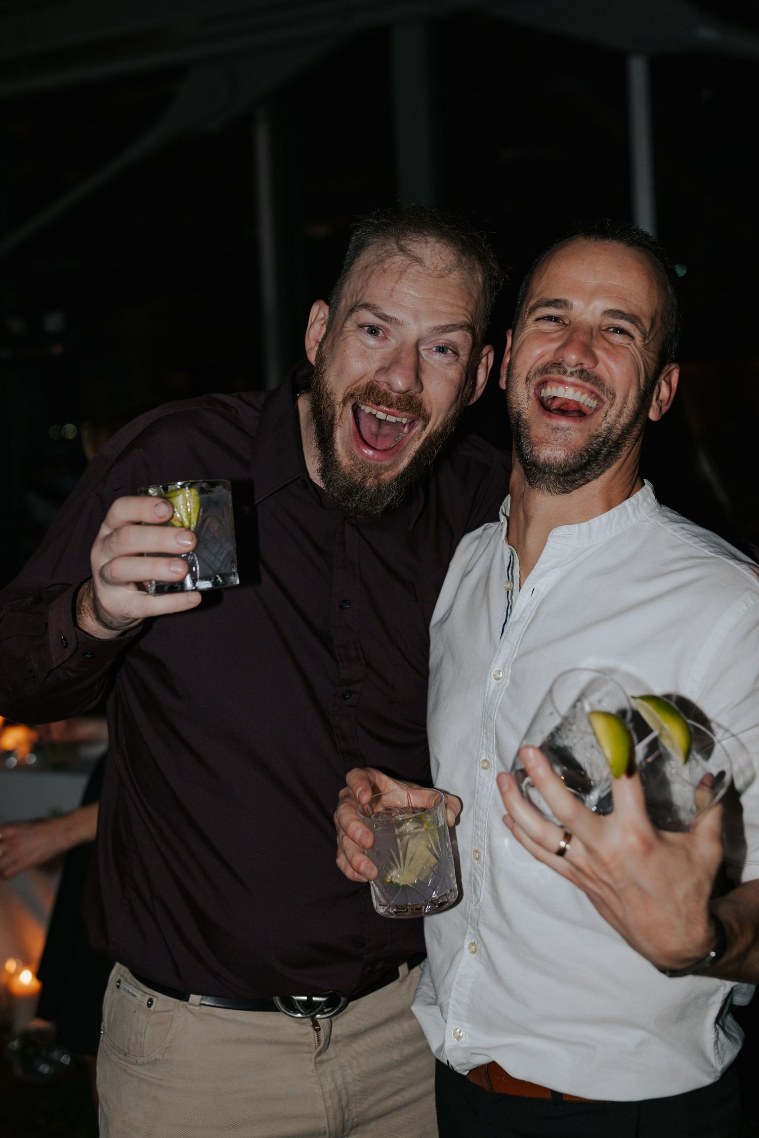 Two party guests laugh while holding drinks at a nighttime reception.