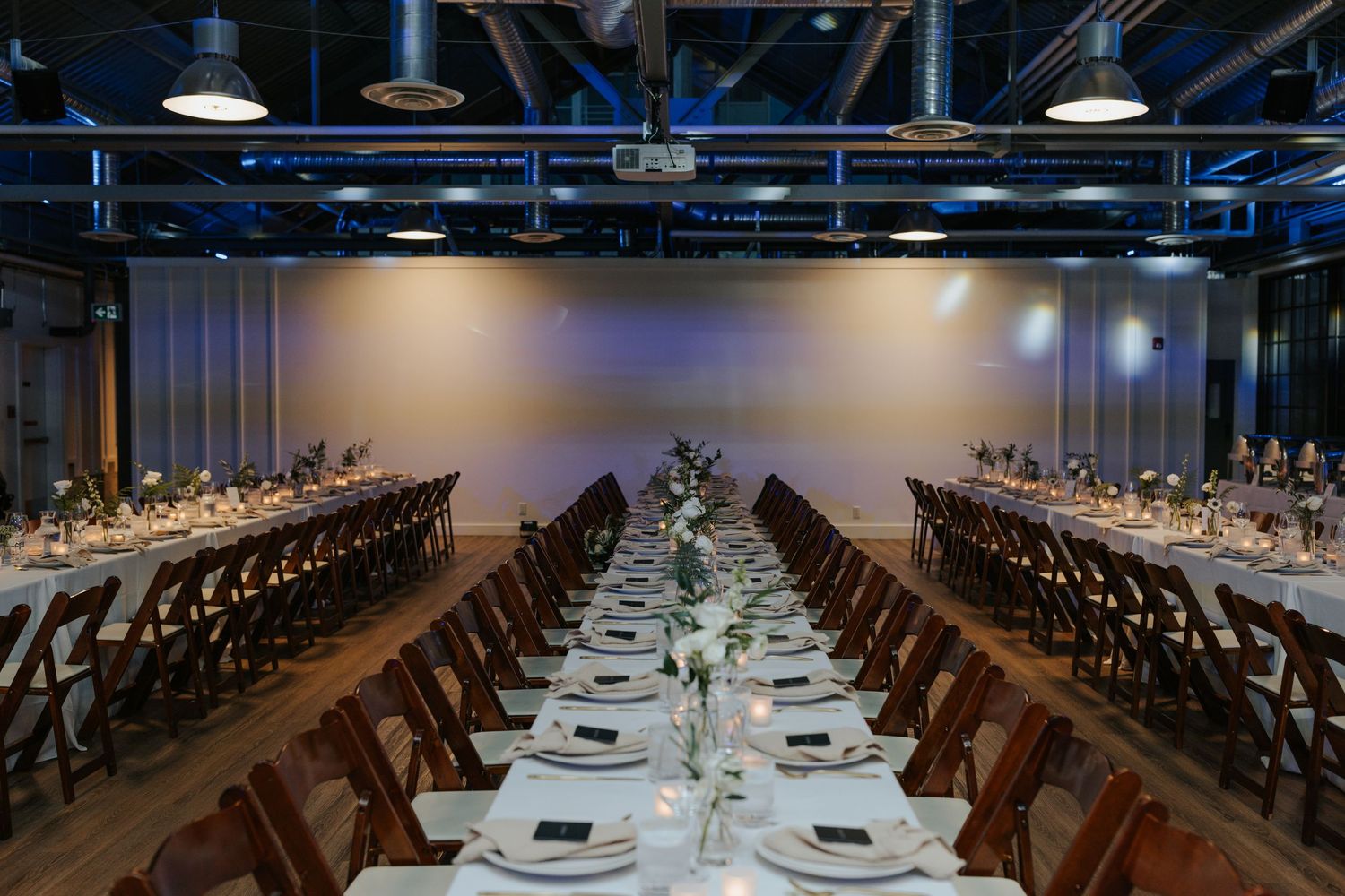 Long banquet tables set for a formal wedding reception with elegant place settings and modern decor.