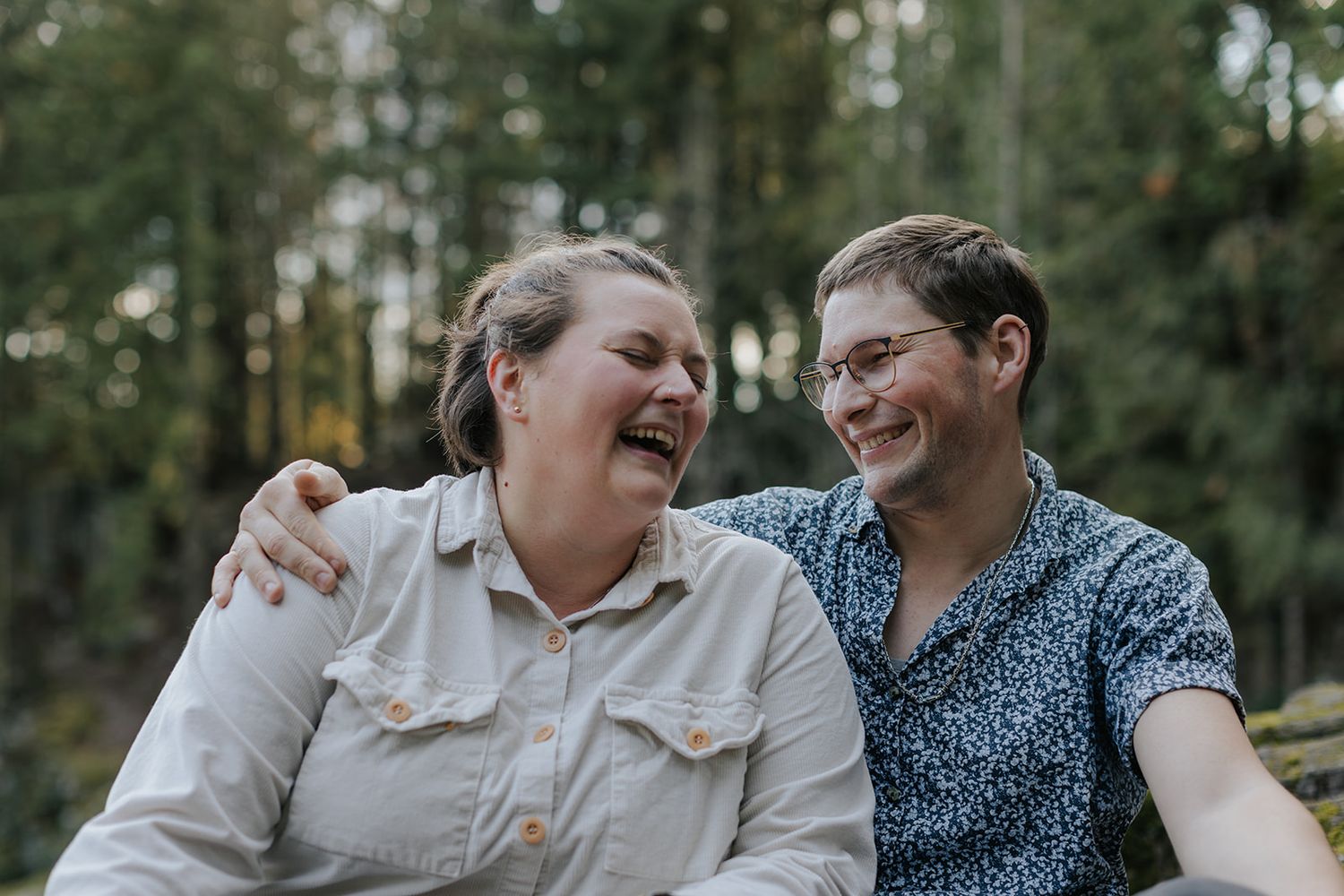 A joyful couple shares intimate moments while laughing together in a lush forest setting.