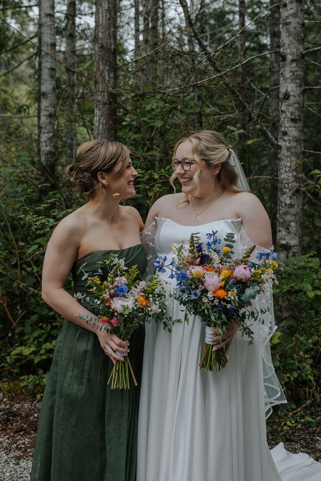 Two people share an intimate moment while holding beautiful wildflower bouquets in a forest setting.