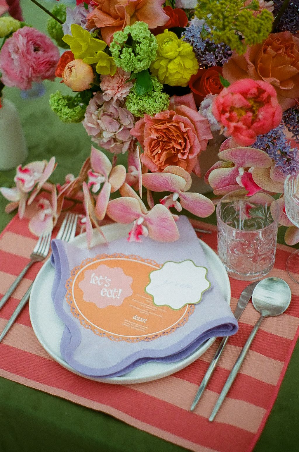 Place setting with coral charger plate and lush floral centerpiece at wedding reception.