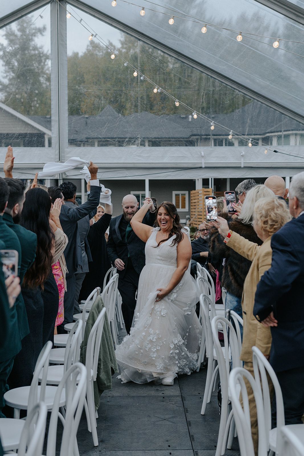 Wedding reception celebration in a clear tent with string lights and dancing guests.