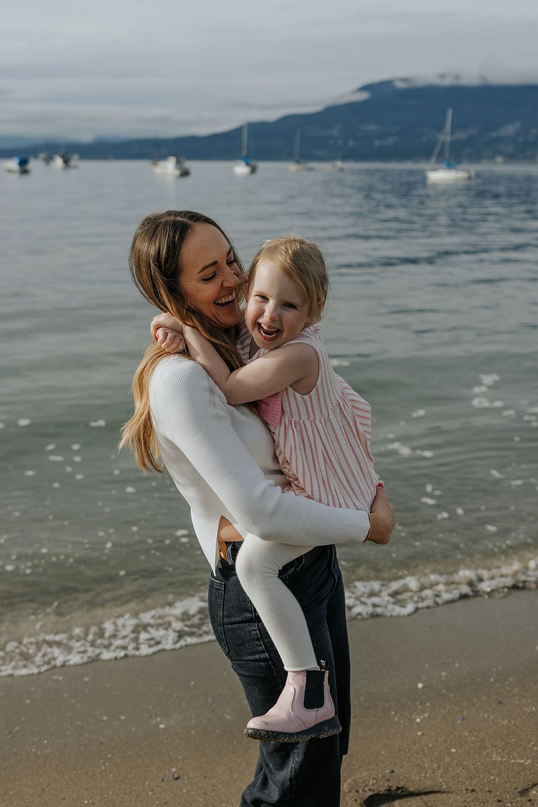 Joyful moment shared between parent and child at the beach with mountains in background.
