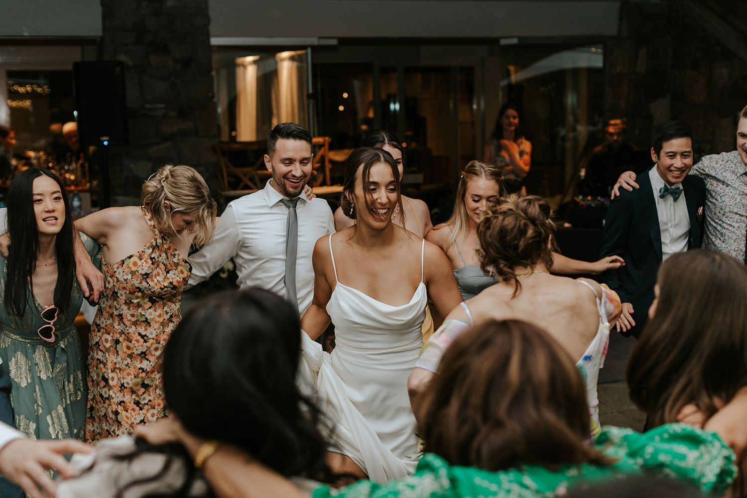 Wedding reception guests dancing and celebrating in a dark indoor venue.