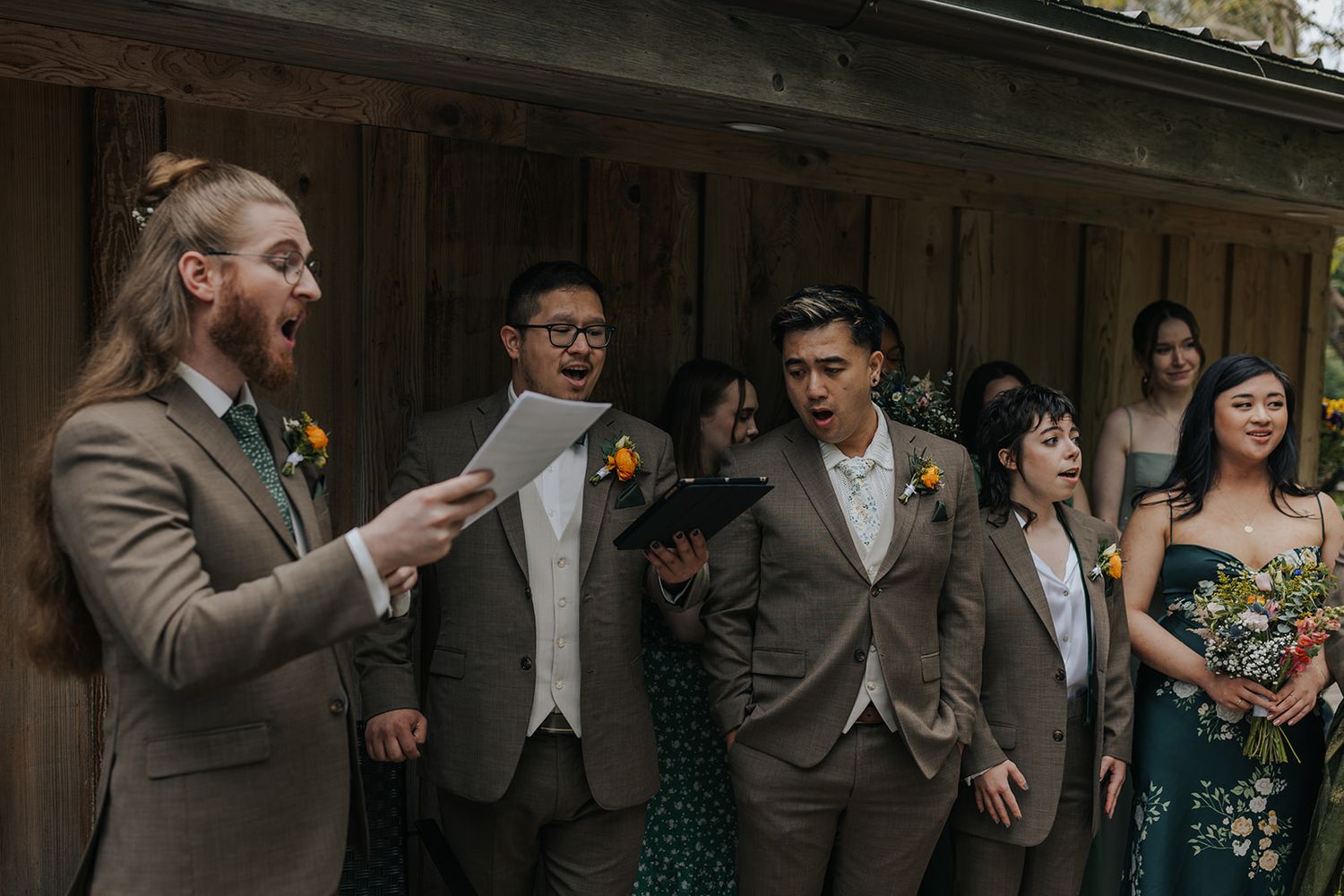 Wedding party members lined up on rustic wooden deck during ceremony.