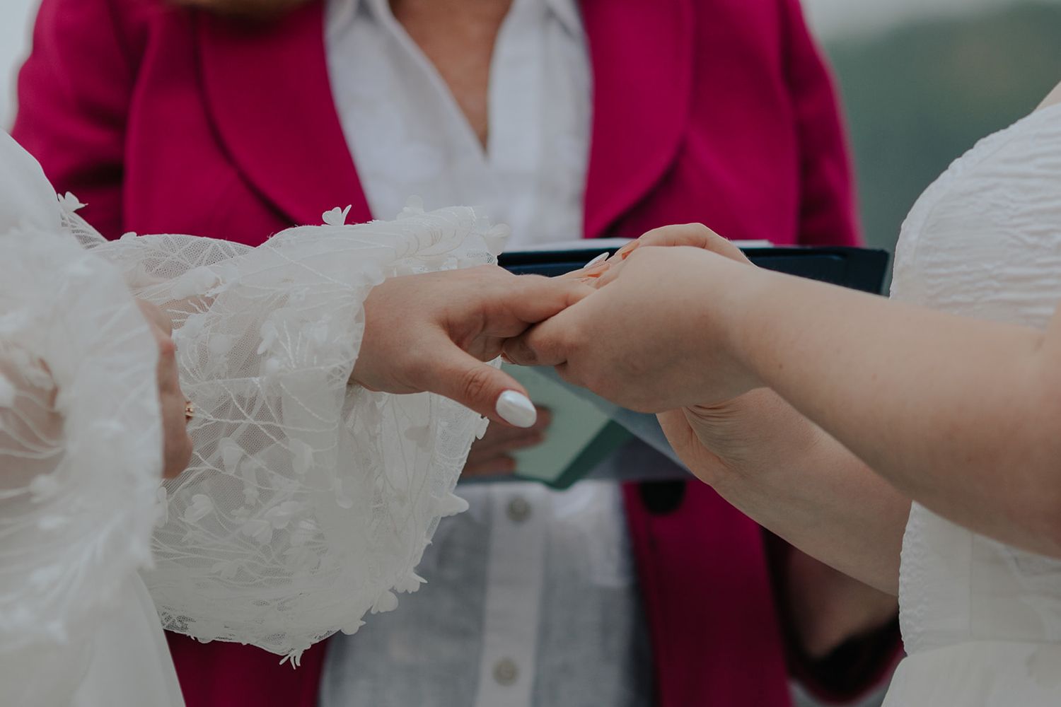 Exchange of wedding documents between officiant in pink and couple during ceremony.