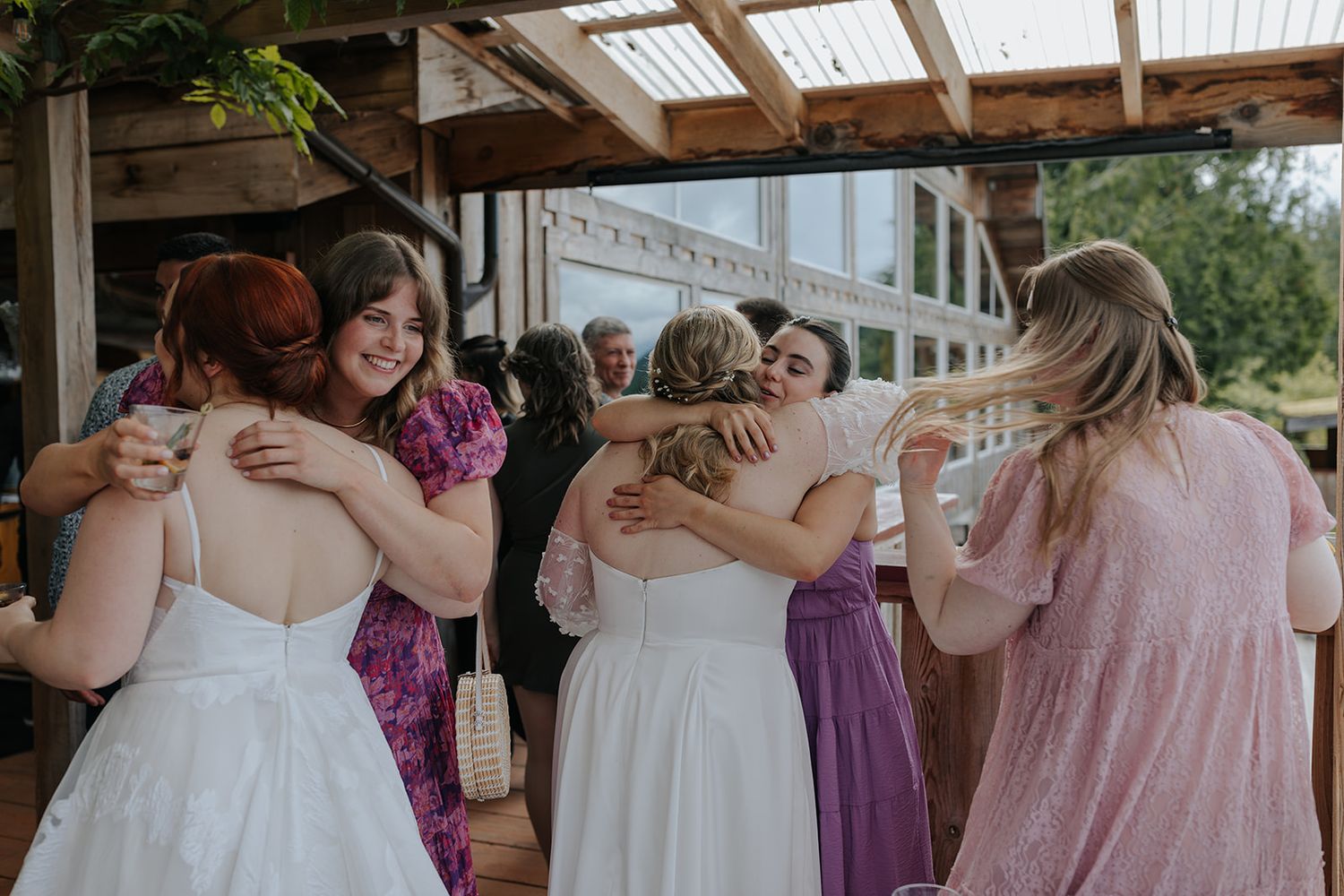 Wedding party in purple and pink dresses sharing emotional embraces at an outdoor venue.