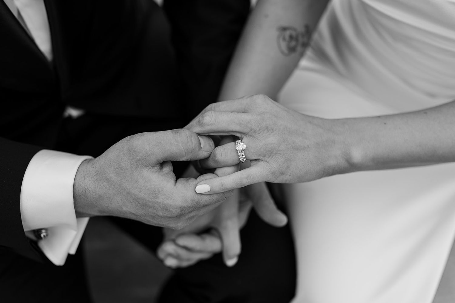 Close-up black and white photo of hands exchanging wedding rings during a ceremony.