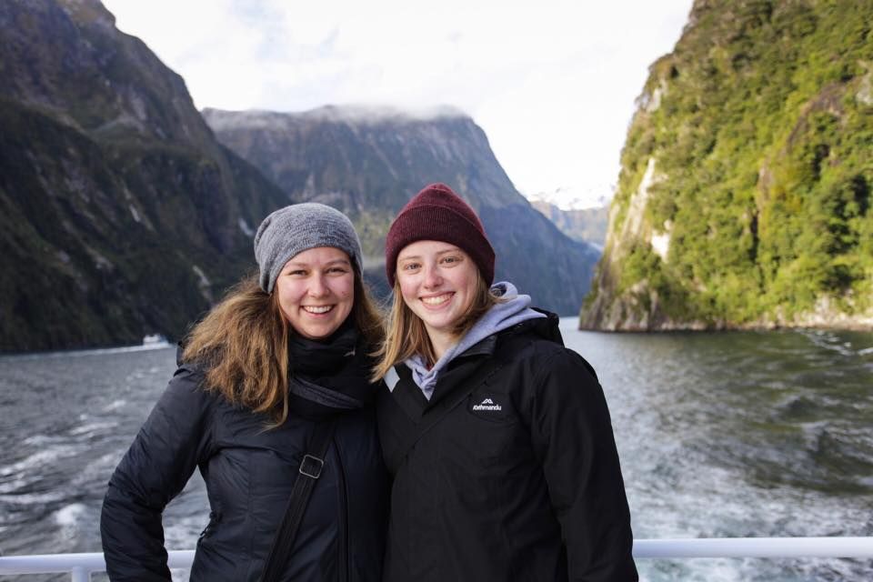 Scenic views of mountains and water at Milford Sound with tourists posing for photos.