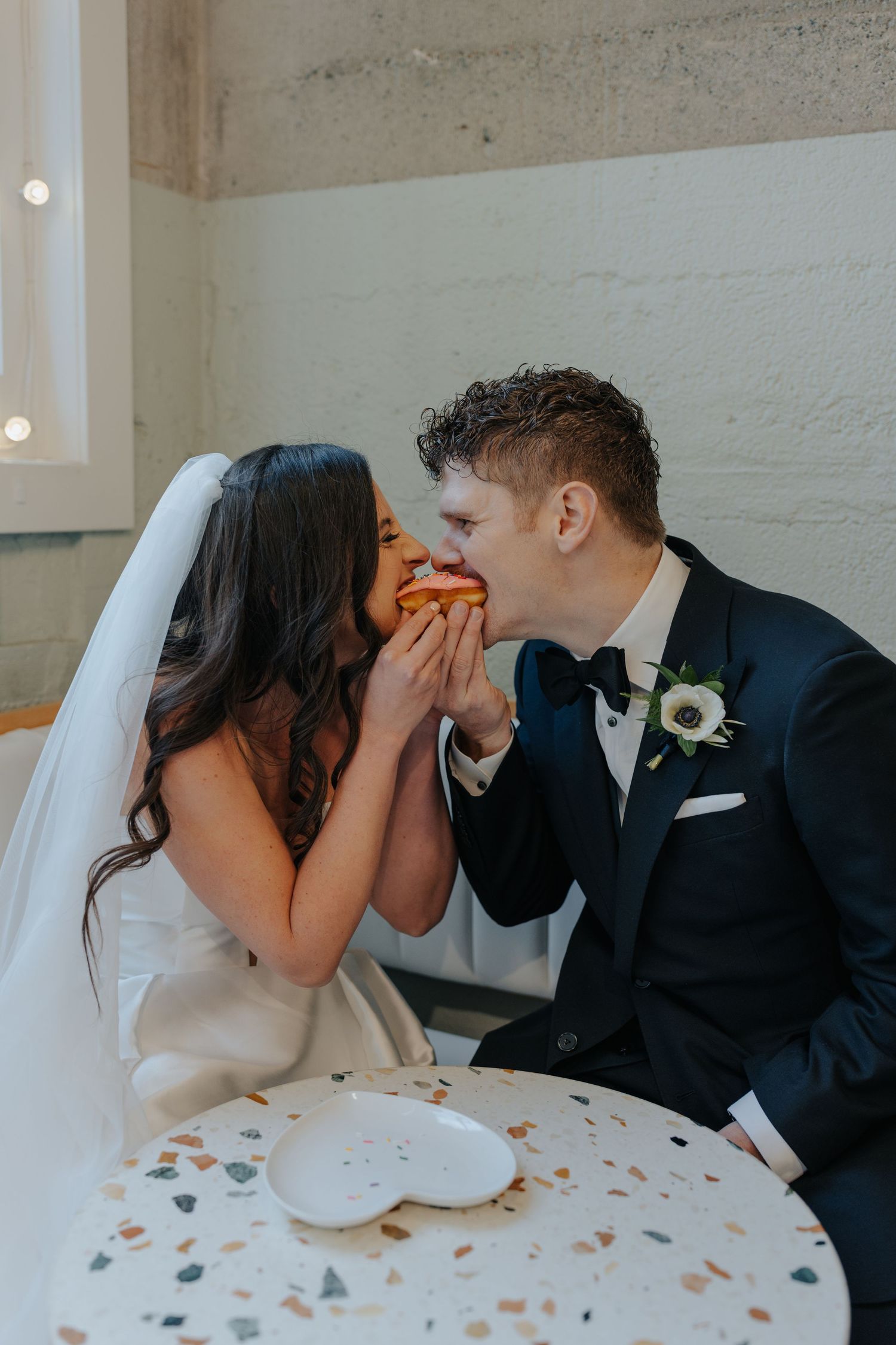 A couple shares a sweet moment while sitting at a table during their wedding celebration.
