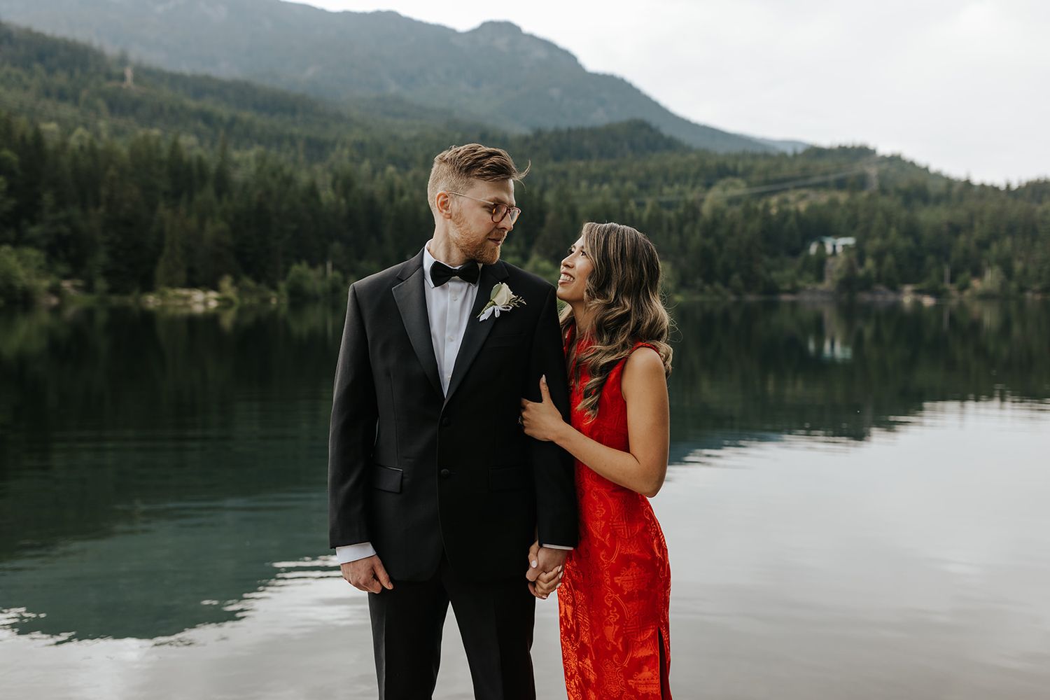 Couple posing against mountain lake backdrop in formal attire.